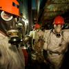 Рабочие, одетые в противогазы и пластиковые костюмы для защиты от радиационного излучения, направляются на свое место работы 