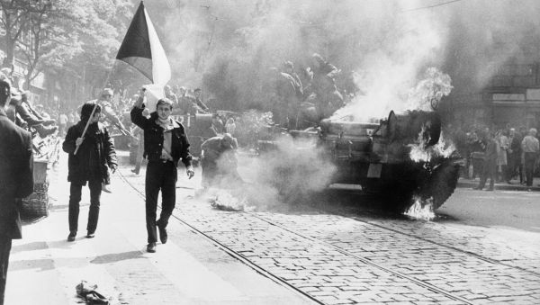 Фото:  Протестувальники з прапором Чехословаччини на тлі підпаленого совєтського